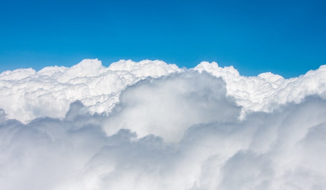 An aircraft crossing a bright sky between clouds